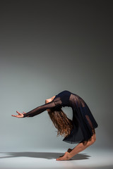 Young beautiful dancer in black dress posing on a dark gray studio background