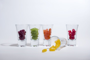 Multi coloured jelly beans in small clear glasses on a white background. 