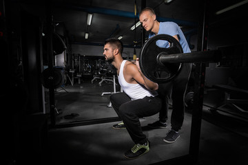 Fototapeta na wymiar Muscular young man is working out in gym with his fitness instructor
