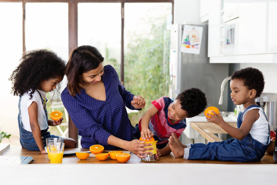 Une maman et ses enfants pr&eacute;parent du jus d'orange dans la cuisine