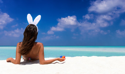 Frau mit Hasenohren und Ostereiern am tropischen Strand