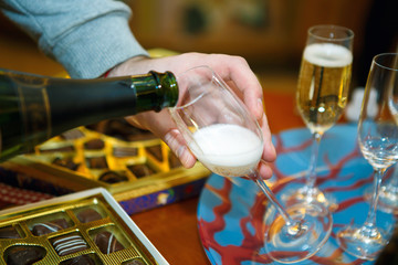 Male hand pouring champagne into a glass. Festive table with alcohol and sweets. Drinking at the Banquet.
