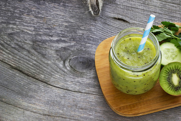 Green smoothie with kiwi fruit, cucumber, mint and parsley on old grey wooden desk
