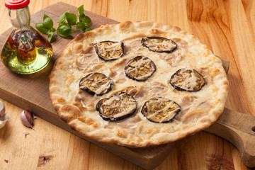 Pizza with eggplant, cheese and pork on a wooden cutting board.
