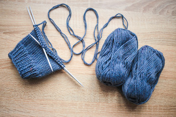 Knitting needles and blue yarn are on the table. Wooden background. Hobbies 