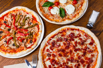 Several different pizzas on a wooden restaurant table.