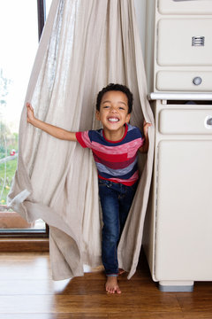 Un enfant joue &agrave; se cacher derri&egrave;re les rideaux du salon