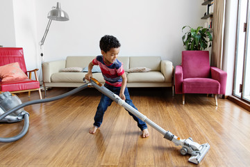 Un enfant passe l'aspirateur dans le salon en souriant