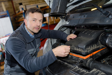 smiling mechanic repairing car engine in a garage