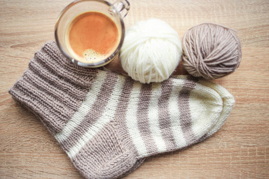 Beige and white yarn, beige-beige sock and black coffee are on the table. Wooden background. Hobbies 