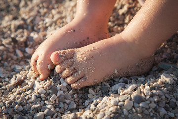 Children's feet. Baby sits and play on beach by sea in pebbles and sand.