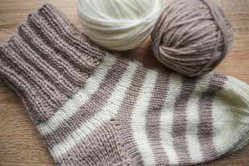 Fototapeta na wymiar Beige and white yarn, Knitted striped beige-beige sock are on the table. Wooden background. Hobbies 