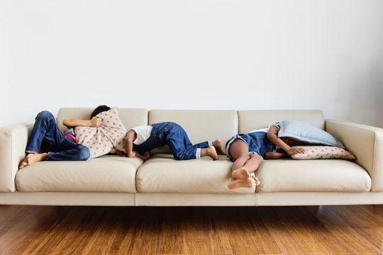Trois enfants se cachent sous les coussins du canap&eacute;