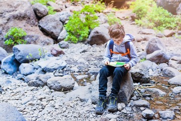 Little boy child reading map on mountain trail.