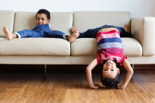 Un enfant se met la t&ecirc;te &agrave; l'envers sur le canap&eacute; son petit fr&egrave;re &agrave; c&ocirc;t&eacute; de lui