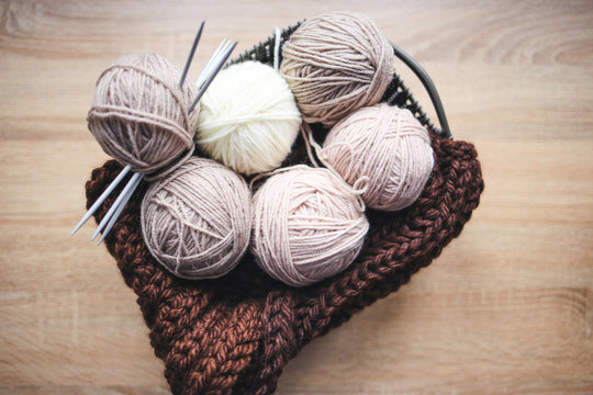 Beige yarn, knitting needles and a brown scarf are in the basket. Wooden background. Hobbies 