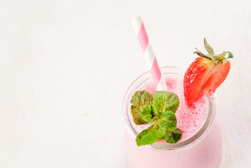 Summer dessert or breakfast - strawberry milkshake with mint, in a small jar, with a striped tube. On a white table. copy space