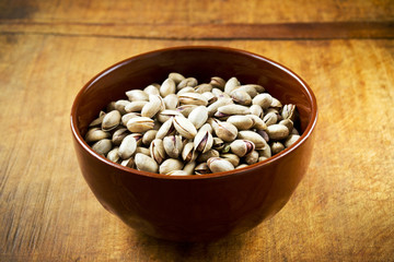 Pistachio nuts in a dark bowl on wooden table, ready to eat
