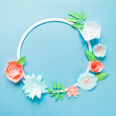 Round frame with color paper flowers on the blue background. Flat lay. Nature concept