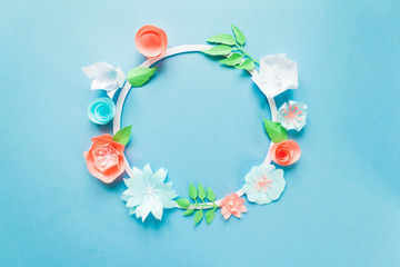 Round frame with color paper flowers on the blue background. Flat lay. Nature concept