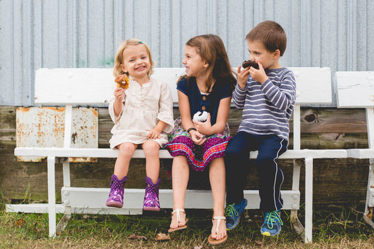 Children sitting bench eating donuts