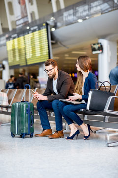 Elegant business couple sitting with phone and book at the waiting hall in the airport. Business travel concept
