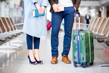 Elegant business couple with suitcase, phone and tickets standing at the airport. Close up view on the legs