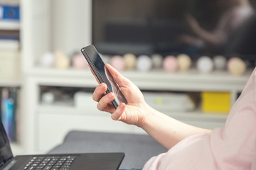 Close-up of female hands using smart phone while working on computer at home