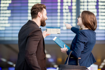 Business couple looking at the timetable holding boarding pass at the airport