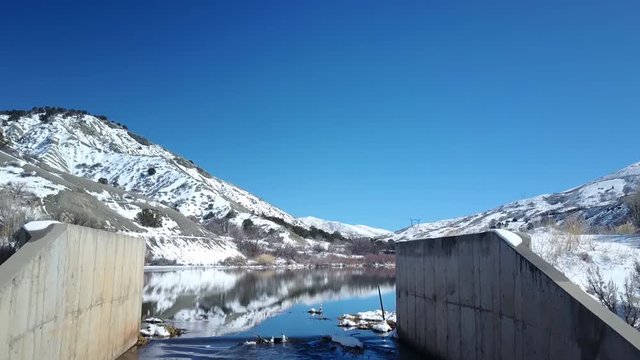 Aerial dam spillway to mountain lake winter snow. Beautiful blue water and valley lake spillway to avoid floo ids and storage capability. Valley. Snow on ground during late winter and early spring.