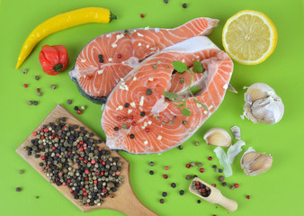 Fresh salmon steaks surrounded with spices on green kitchen mat