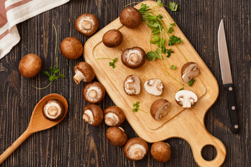 Sliced Royal Champignons with greens on wooden cutting board with kitchen knife on black rustic background, top view. Vegan or vegetarian healthy food concept