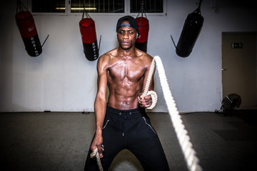 Portrait of young determined man waving battle ropes during high-intensity training indoors