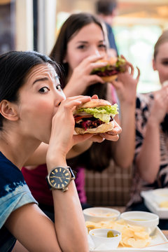 Portrait of three young women eating hamburgers