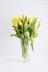 Yellow tulips in vase on white wooden table
