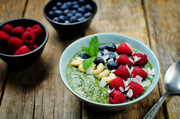 Spinach smoothies breakfast bowl with coconut flakes, raspberry, blueberry and cashews