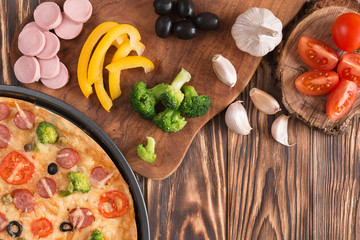 pizza with broccoli, peas, sausage, olives, peppers and tomatoes on a wooden table