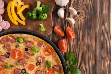 pizza with broccoli, peas, sausage, olives, peppers and tomatoes on a wooden table