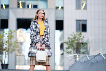 Blond hair young woman in check skirt against modern building. Street fashion style concept.