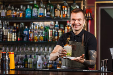 Cheerful bartender gives the cocktail to customer.