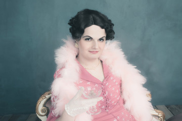 Transgender woman vintage 1920s fashion sitting on sofa holding champagne glass.