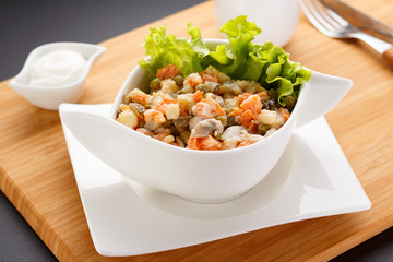 Russian salad Olivier on a white plate, wooden board and background.