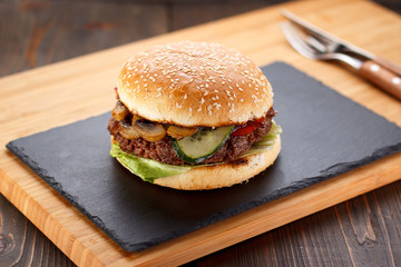 Big burger on a stone plate and wooden background.