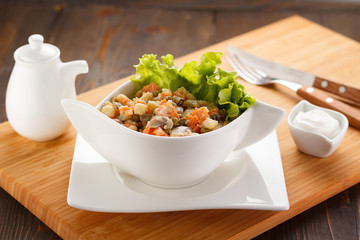 Russian salad Olivier on a white plate, wooden board and background.