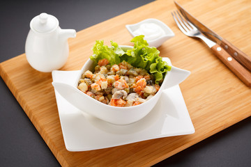 Russian salad Olivier on a white plate, wooden board and background.