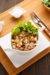 Russian salad Olivier on a white plate, wooden board and background.