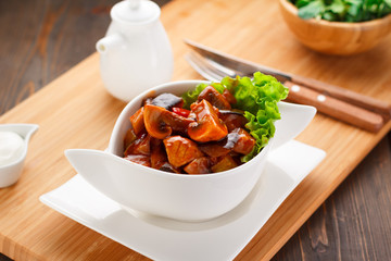 fried mushrooms in sauce on a white plate, wooden board and background.