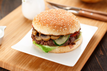 Big burger on a white plate, wooden board and background.