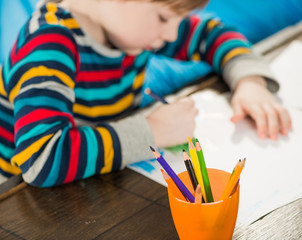 boy drawing picture on a table with colorful pencils