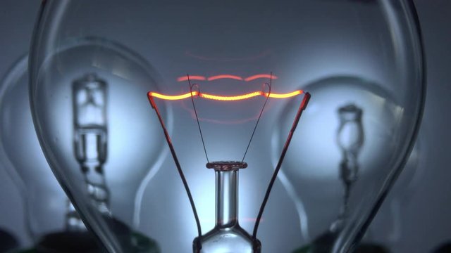 Close up of a filament in a light bulb switching on and off slowly with two halogen bulbs in the background.